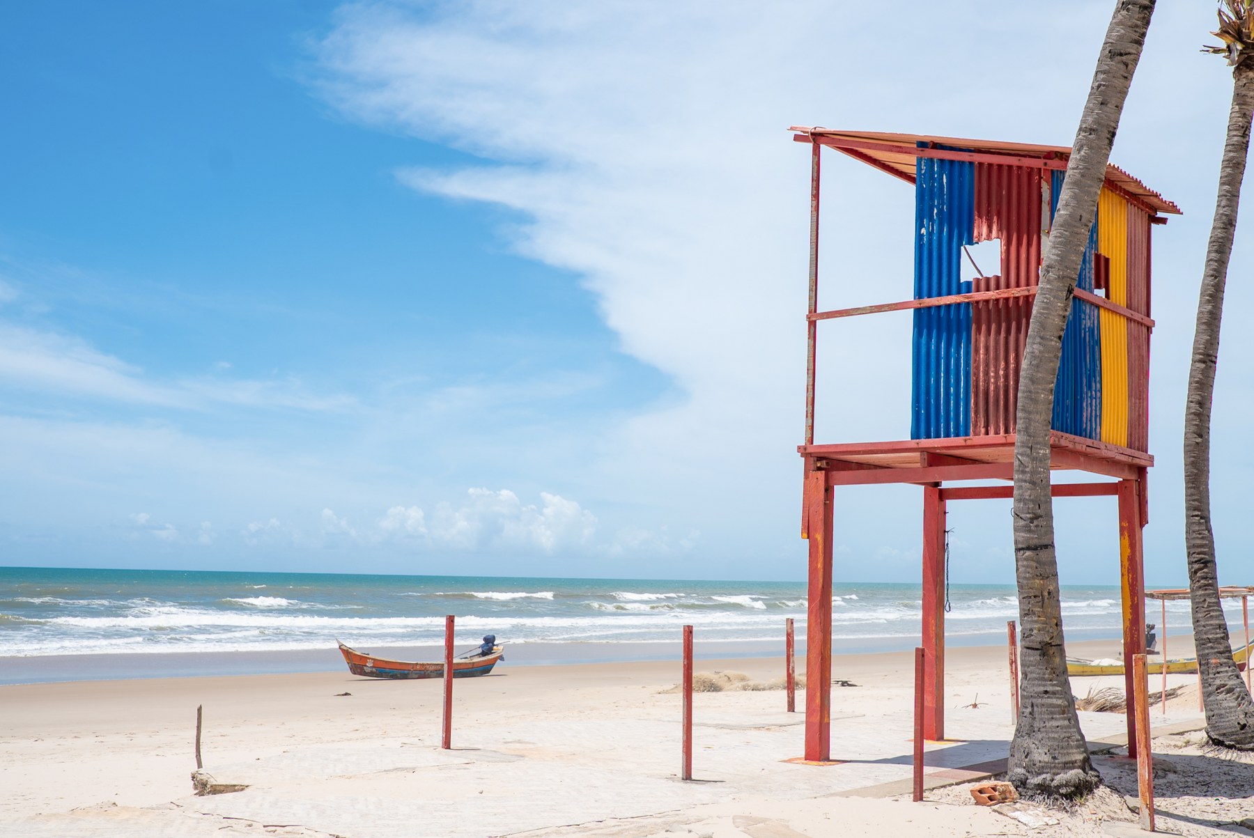 Praia do Abaís, com faixa de areia, mar, barco e posto de guarda-vidas colorido